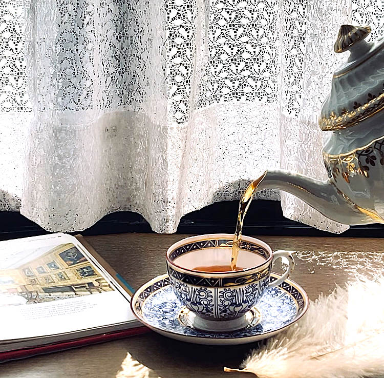 温かい光が差し込む窓辺のカップに紅茶を注ぐ